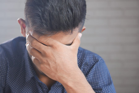 Close up of sad man covering face with hand.の写真素材
