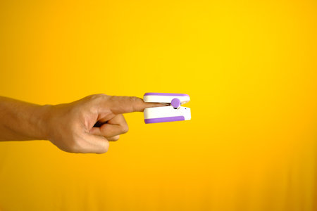 close up of man hand using pulse oximeter against yellow backgroundの写真素材