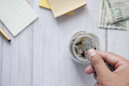 young man saving coins in a jar white sitedの写真素材