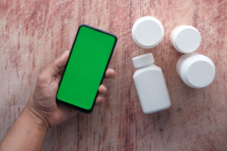 many pill container and hand hold a smart phone on wooden tableの写真素材