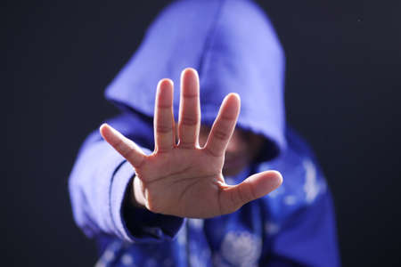 sad man in hood cover face with hands isolated in black.の写真素材