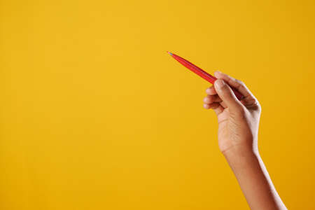 holding a red color pencils against yellow backgroundの写真素材