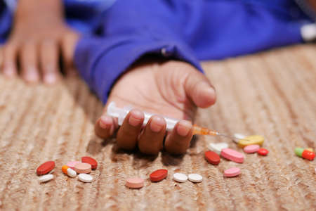 drug addiction concept with hand holding pills and syringe laying on floorの写真素材
