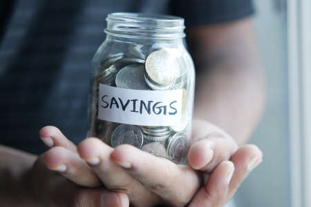 young man saving coins in a jar white sitedの写真素材
