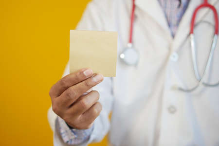 doctor hand hold a sticky note against yellow backgroundの写真素材