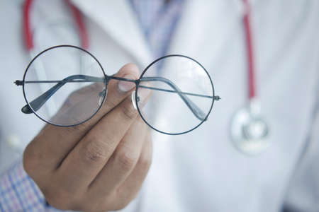 doctor hands giving pair of black glasses to patient.の写真素材