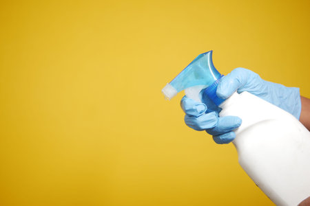 hand in blue rubber gloves holding spray bottle with copy space