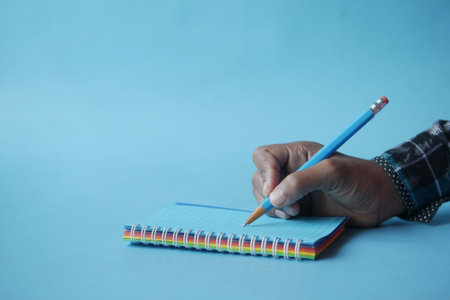 man hand writing on notepad while sited