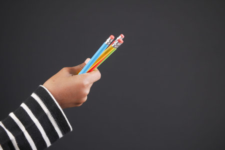 child girl holding many color pencils against gray background