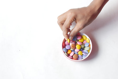 child boy picking multi-colored sweet candies in a bowl on white backgorundの写真素材