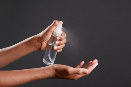 close up of young man hand using hand sanitizer spray isolated on blackの写真素材