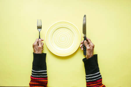 senior women holding cutlery and empty plate on yellow backgroundの写真素材