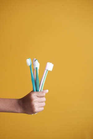 holding many colorful tooth brush against yellowの写真素材