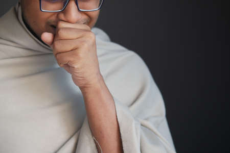Mature man in blanket coughing while sited on bedの写真素材