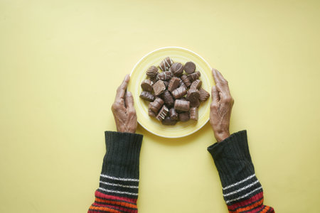senior women eating dark chocolate on a plate on yellow backgroundの写真素材