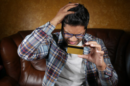 upset man holding credit card while sited on sofa