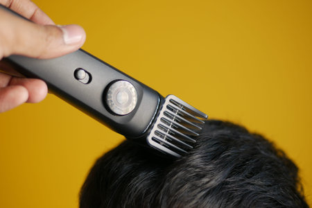 cutting hair with a hair-clipper on yellow background