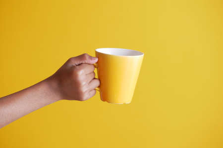 close up of man hand holding mug isolated on yellowの写真素材