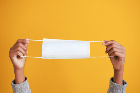 man hand holding surgical face mask against yellow background