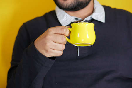 young man hand holding a yellow color coffee mugの写真素材