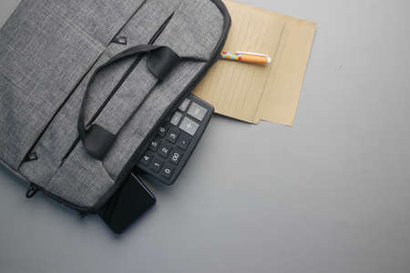 Top view of note pad, calculator, pen in a office bag on gray backgroundの写真素材