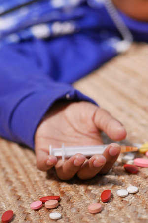 drug addiction concept with hand holding pills and syringe laying on floor