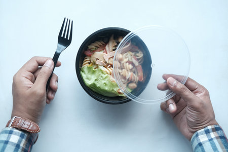 young man eating fresh vegetable salad in a plastic bowl