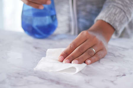 hand in blue rubber gloves holding spray bottle cleaning tableの写真素材