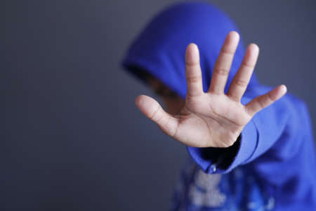 sad man in hood cover face with hands isolated in black.の写真素材