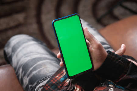 young man hand using smart phone with green screen sitting on a sofaの写真素材