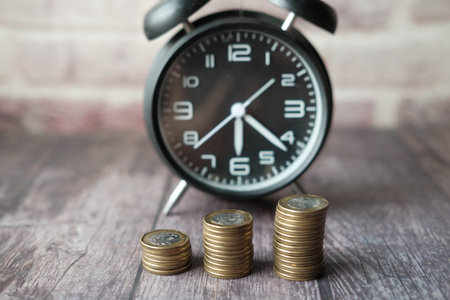 old alarm clock and stack of coins on table