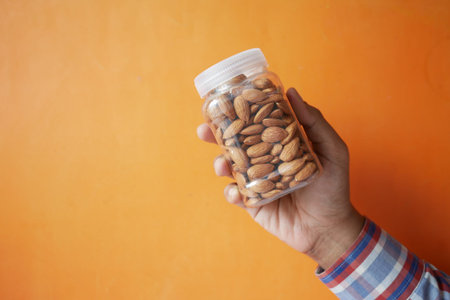 holding a almond nuts jar against orange backgroundの写真素材