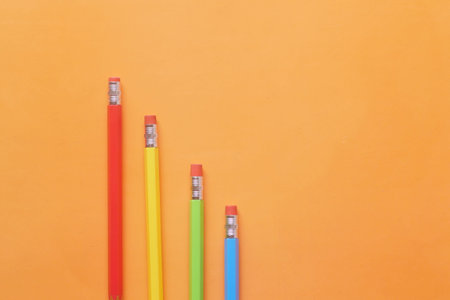 flat composition of colorful pencils on orange background