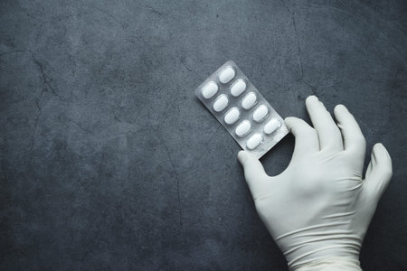 flat composition of hand in gloves holding a blister pack on black background