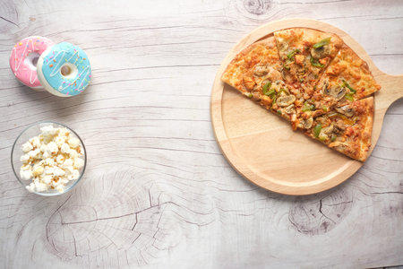 Slice of cheese pizza on a plate , donuts and popcorn on pink