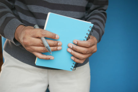 man hand holding a blue color notepad with pen
