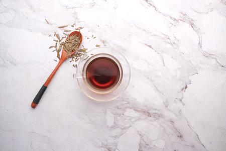 Dry tea leaves on spoon and green tea on tiles background