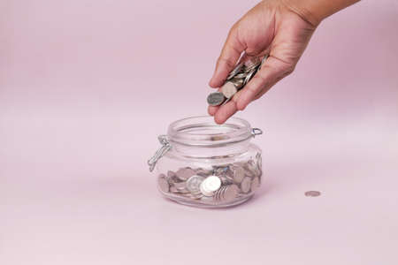 young man saving coins in a jar white sitedの写真素材
