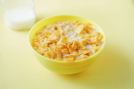 corn flakes and milk in a yellow color bowl