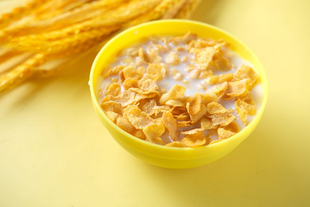 pouring milk in corn flakes on yellow background