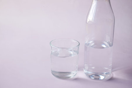 glass of drinking water on light pink background