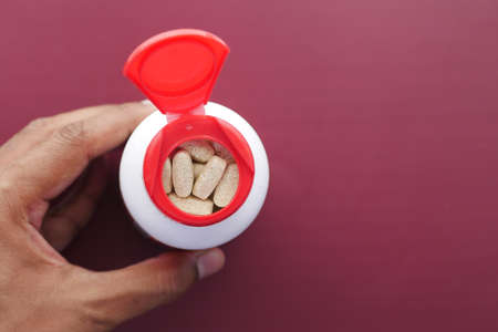 young man hand holding medicine pill container on red background top viewの写真素材