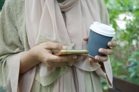women hand holding smart phone and paper coffee cupの写真素材