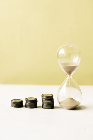 hourglass and stack of coins on table,