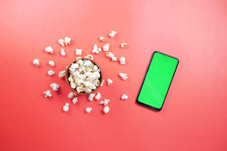 top view of smart phone and popcorn on red backgroundの写真素材
