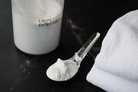 Washing powder in plastic spoon and towel on black background