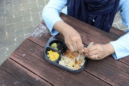 women eating chicken rice in a take away packet in park bench