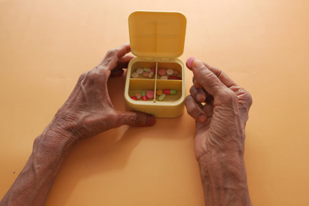 senior women taking medicine from a pill box on orange background