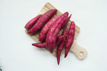 raw sweet potato on chopping board on white backgroundの写真素材