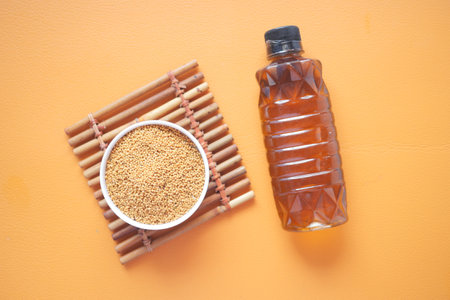 Mustard oil in a plastic jar and seed on orange backgroundの写真素材
